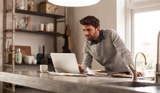Man using laptop in well-lit home office with LED task lighting for efficient remote work setup.