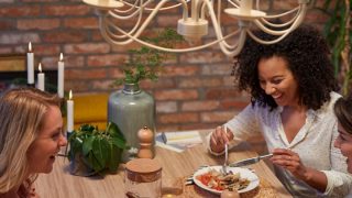 Modern kitchen with vintage style LED pendant lights illuminating two women enjoying dinner, creating warm, inviting atmosphere.