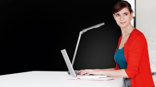 Woman studying at desk with adjustable LED task lamp, providing optimal illumination for homework in colorful home learning space.